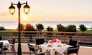 Udsigt over et bord med morgenmadsservering på en terrasse med havet i baggrunden. (AI-genereret tekst)