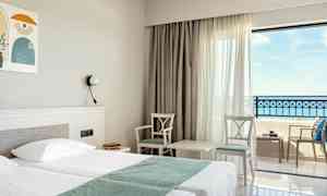 Hotelværelse med dobbeltseng, to stole og et bord ved vindue med havudsigt. (AI-genereret tekst)