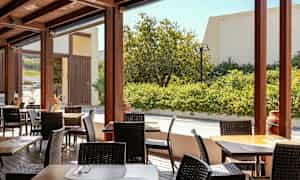 En udendørs terrasse med borde og stole, omgivet af planter. (AI-genereret tekst)