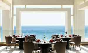 En moderne restaurant med udsigt over havet, møbleret med runde borde og behagelige stole. (AI-genereret tekst)