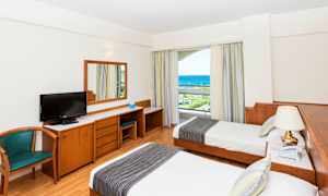 Hotelværelse med to enkeltsenge, skrivebord, stol og havudsigt. (AI-genereret tekst)