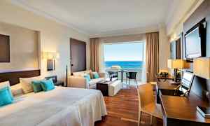 Hotelværelse med dobbeltseng, siddeområde og udsigt til havet. (AI-genereret tekst)