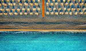 Luftfoto af en strand med parasoller og liggestole, med havet i forgrunden. (AI-genereret tekst)