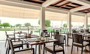 Udendørs restaurant med borde og stole, omgivet af grønt. (AI-genereret tekst)