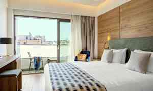 Et hotelværelse med en stor seng, skrivebord, stol og altan. (AI-genereret tekst)