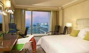 Hotelværelse med en dobbeltseng, stole og udsigt over altaner og havet gennem store vinduer. (AI-genereret tekst)