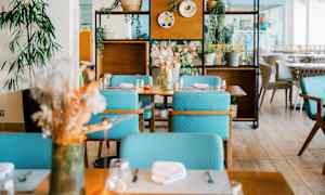 Et moderne indrettet restaurantområde med borde, turkise stole og dekorative planter. (AI-genereret tekst)