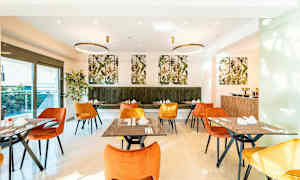 En spisesal med orange og gule stole samt grøn polstret bænk. Bordene er dækket og dekoreret. Væggene har billeder af planter. (AI-genereret tekst)