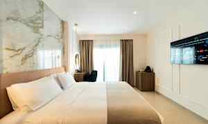 Hotelværelse med opredt seng, væg-TV og skrivebord nær et vindue. (AI-genereret tekst)