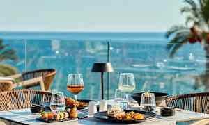 Et dækket bord med mad og drikke på en terrasse med udsigt over havet. (AI-genereret tekst)