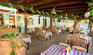 Restaurant med udendørsborde dækket med rødhvidternet dug. (AI-genereret tekst)