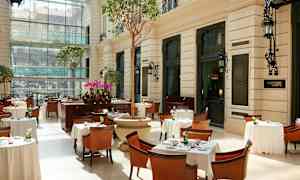 En lys restaurant med borde, stole og planter i et indglasset miljø. (AI-genereret tekst)