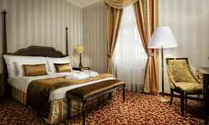 Et elegant hotelværelse med en stor seng, stol og vindue med gardiner. (AI-genereret tekst)