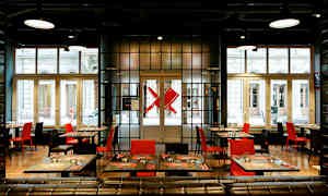 Moderne restaurant med røde og sorte stole samt dækkede borde foran store vinduer. (AI-genereret tekst)