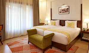 Et hotelværelse med to separate senge, en grøn bænk og en lys vinduesgardin. (AI-genereret tekst)