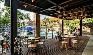 En udendørs servering med borde og stole samt en pool i baggrunden. (AI-genereret tekst)