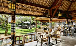 En restaurant med udendørs siddepladser, omgivet af grønt. (AI-genereret tekst)