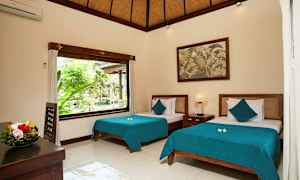 Et lyst og stilrent indrettet soveværelse med to senge med blå sengetæpper. Et stort vindue lader naturligt lys komme ind og viser grønne omgivelser udenfor. En frugtskål står på bordet, og et maleri hænger på væggen. (AI-genereret tekst)