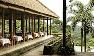 En udendørsrestaurant med stråtag og dækkede borde, omgivet af frodig vegetation. (AI-genereret tekst)