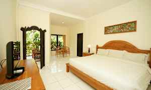 Et velindrettet og lyst soveværelse med en stor seng, træsdetaljer og siddeområde nær vinduer med udsigt til grønne omgivelser. (AI-genereret tekst)