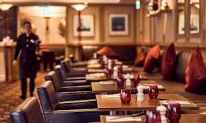 En restaurant med dækkede borde, røde glas og mørke stole kan ses på billedet. (AI-genereret tekst)