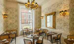 En restaurantinteriør med klassisk indretning, borde og stole, stor spejl og en lysekrone. (AI-genereret tekst)