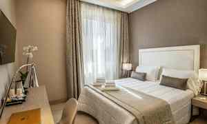 Et hotelværelse med en dobbeltseng med hvidt og beige sengetøj, et skrivebord med en lampe og et vægmonteret TV. (AI-genereret tekst)