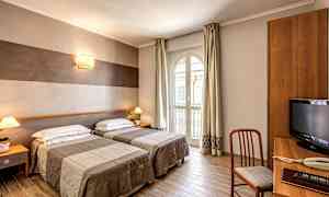 Et hotelværelse med to enkeltsenge, et skrivebordshjørne og et stort vindue, der lukker dagslys ind. (AI-genereret tekst)