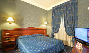 Et hotelværelse med blå indretning, herunder seng, gardiner og tapet, samt et fjernsyn ved siden af. (AI-genereret tekst)