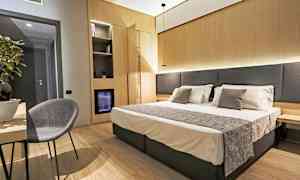 Hotelværelse med dobbeltseng, natbord og en stol ved et bord. (AI-genereret tekst)