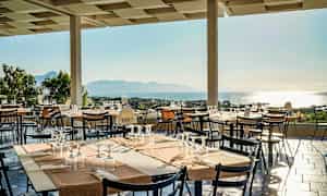 Terrasse med dækkede borde og udsigt over havet. (AI-genereret tekst)