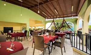 Udendørs spiseområde med dækkede borde med røde duge, stole og en grøn væg i baggrunden. (AI-genereret tekst)