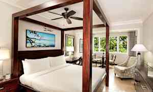 Et hotelværelse med en himmelseng, en siddegruppe og et stort vindue. (AI-genereret tekst)