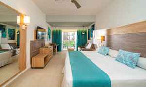 Et hotelværelse med en dobbeltseng og blå detaljer. Der er også en sofa, et skrivebord og en altan med udsigt. (AI-genereret tekst)