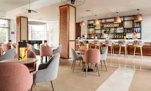 En moderne indrettet café eller bar med borde og stole i forskellige farver samt en oplyst bardisk i baggrunden. (AI-genereret tekst)