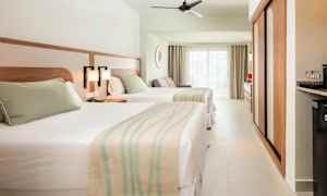 Hotelværelse med to senge, lys indretning og store vinduer. (AI-genereret tekst)