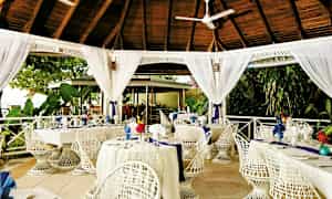 En udendørs restaurant med hvidmalede møbler under et trætak. (AI-genereret tekst)