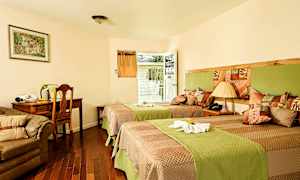 Et hotelværelse med to enkeltsenge, en sofa, et skrivebord og en stol. Der er også en dør, der fører til en altan. (AI-genereret tekst)