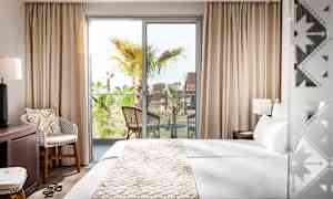 Et hotelværelse med en stor seng, et siddeområde og en balkon med udsigt til palmetræer. (AI-genereret tekst)