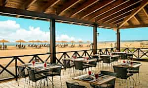 Restaurant med udendørs servering og udsigt over en strand med liggestole og parasoller. (AI-genereret tekst)