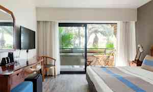 Billede af hotelværelse med seng, skrivebord og balkon med havemøbler. (AI-genereret tekst)