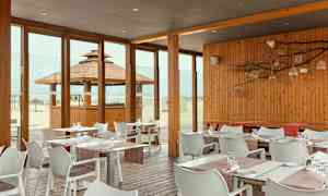 Restaurant med træpaneler og glasvægge med udsigt til stranden. (AI-genereret tekst)