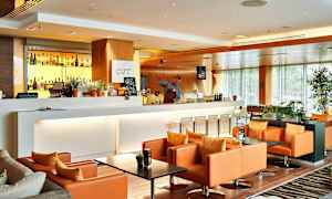 En moderne og elegant lounge med en hvid bardisk, baggrundsbelyste spiritusflasker og komfortable orange lænestole. (AI-genereret tekst)