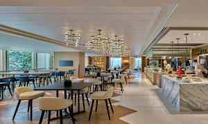 En moderne restaurant med borde, stole og et køkkenområde, hvor to personer arbejder. (AI-genereret tekst)