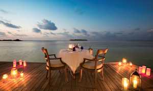 Et bord med to stole står på en træbro ved vandet, omgivet af tændte lys. (AI-genereret tekst)