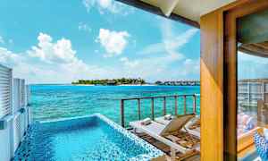 Udsigt fra en terrasse med pool og liggestole mod havet og en ø med bungalows. (AI-genereret tekst)