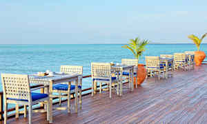 Udendørs servering med borde og stole ved havet. (AI-genereret tekst)