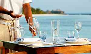 Restaurantpersonale der dækker et bord med vinglas ved en strand. (AI-genereret tekst)