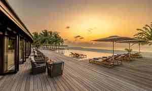 En træterrasse ved en infinity-pool og havet under en aftenhimmel. (AI-genereret tekst)