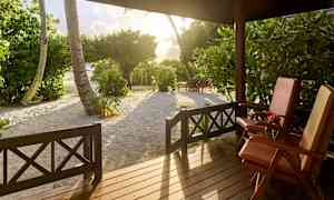 Udsigt fra en veranda med to liggestole, træer og sand i solnedgangslys. (AI-genereret tekst)